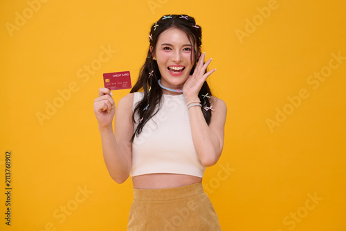 Credit card payment concept with smiling Asian woman presenting a bank card in studio promoting cashless shopping financial freedom online transactions and confident consumer lifestyle.
