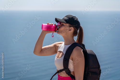 Scenic coastal hike featuring young woman drinking hydration from bright pink water bottle overlooking the ocean