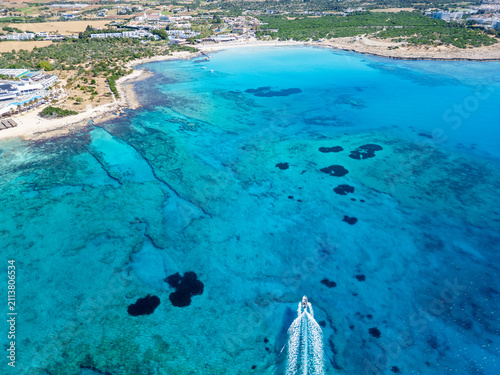 Aerial View of Turquoise Sea and Speedboat Skimming Along Rocky Coastline on Sunny Day, Cyprus, Ayia Napa