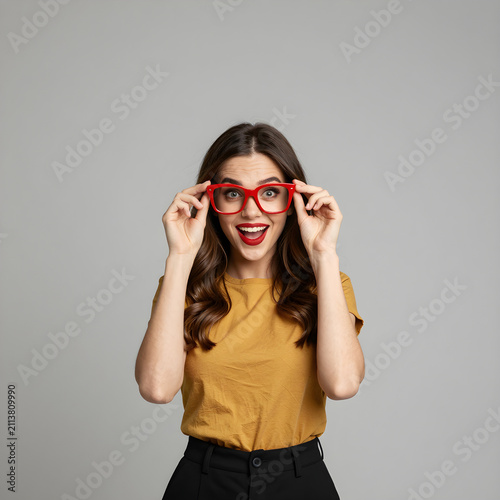 Fashion portrait of a woman wearing oversized red glasses and smiling expressively against a spacious background.
