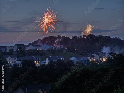 Red and white Independence Day fireworks launching over suburban Pennsylvania homes at dusk