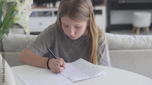 Schoolgirl practicing handwriting and completing writing exercises in a workbook while studying at home