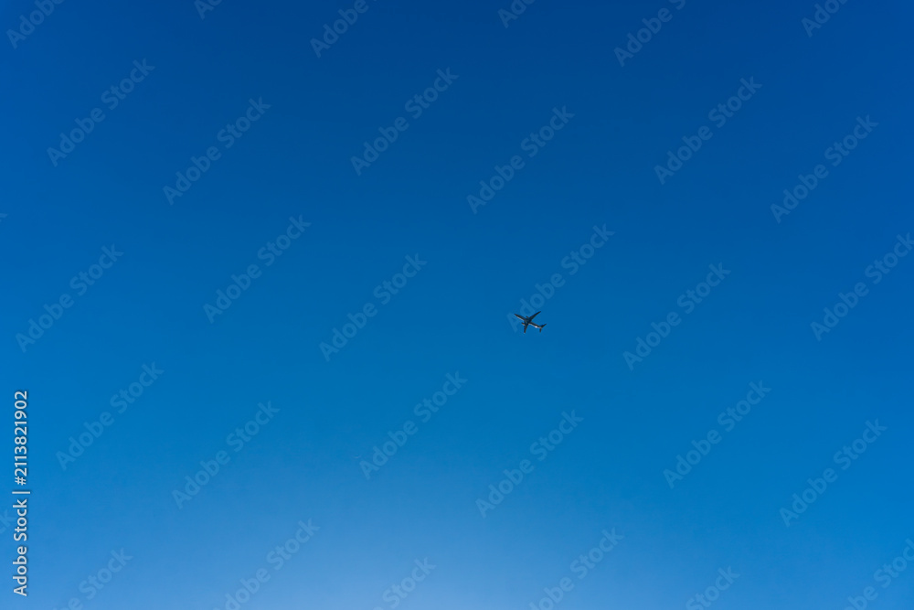 Fototapeta premium Airplane flying across clear blue sky with expansive copy space and minimalist composition highlighting travel, freedom, and aviation concept