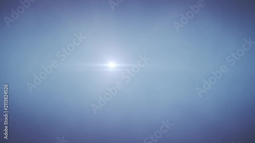 Misty blue sky with bright sunburst and soft lens flare. Light rays pierce through haze