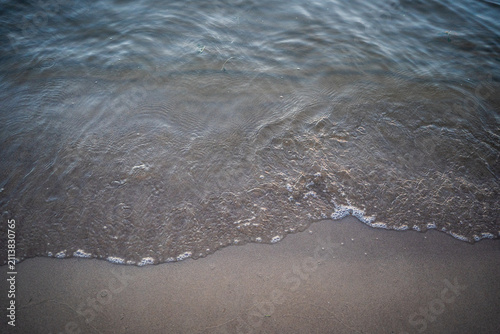 Bild auf Leinwand Delicate ocean waves lapping onto wet sandy shore.