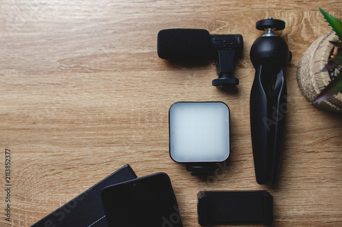 Content creator's essential smartphone vlogging kit. Including a microphone. Portable led light. Mini tripod. And power bank. Is arranged on a wooden desk