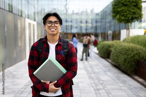 Smiling university student holding books on campus pathway. Copy space.