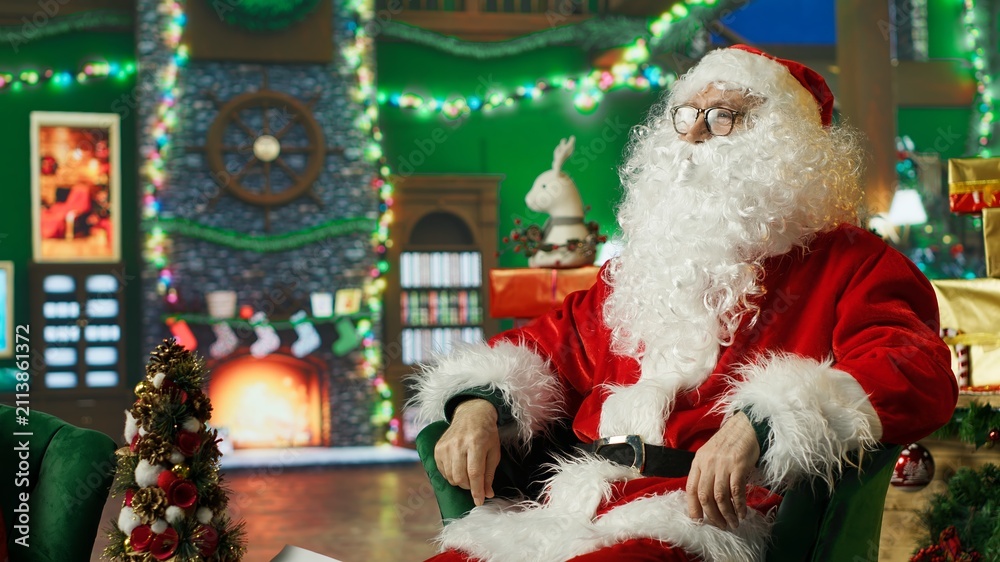 Obraz premium Santa Claus uses augmented reality technology and an AR hologram to read letters and Christmas wish lists sent by children while wearing a festive holiday costume in a modern seasonal scene.