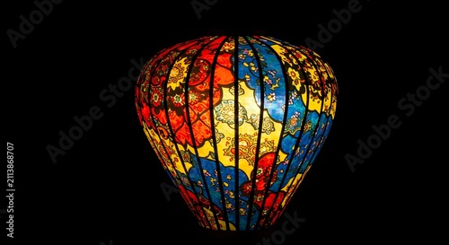 Vibrant colorful traditional Asian silk lantern with floral pattern glowing brightly, isolated on solid black background with copy space.