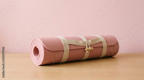 Rolled pink yoga mat on a wooden surface, its textured material and simple straps evoke a sense of calm and readiness for exercise