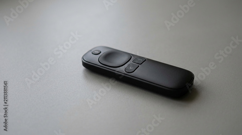 Black remote control with subtle buttons on a neutral, textured surface, representing convenience and modern technology, suitable for media or smart home concepts.