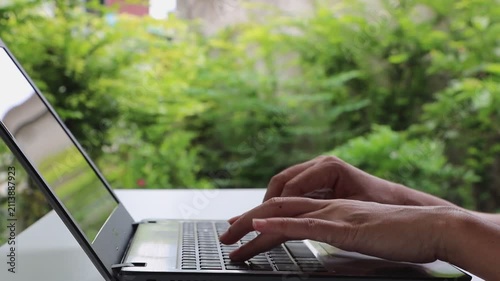 Woman hand typing on computer keyboard. Businesswoman working with laptop on white table in garden at home office or workplace. Remote work, live chatting, online communication, Business technology.