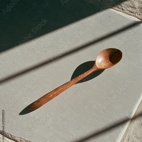 Weathered olive wood spoon casting long shadow on pale stone
