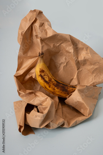 Konstfotografi Overripe banana surrounded by excessive crumpled paper, creating a visual metaphor for wasteful consumption, unnecessary packaging, everyday waste and more conscious use of resources