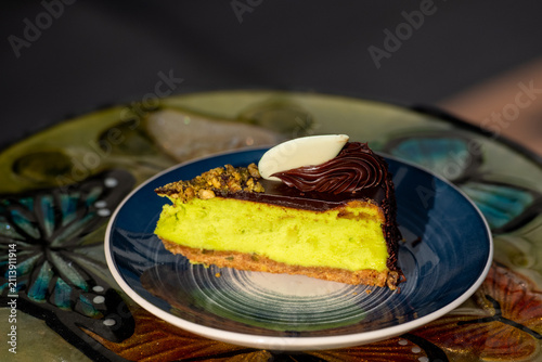 Obraz na plátne A single serving of pistachio brownie cheesecake on a blue and cream colored round plate