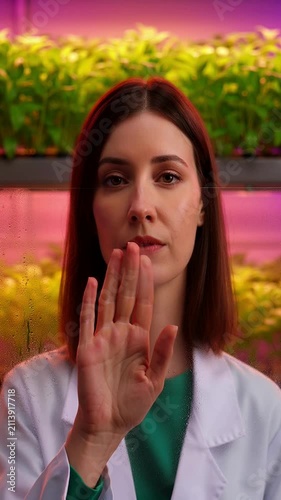 Scientist in White Lab Coat Gesturing in Greenhouse Vertical Farm