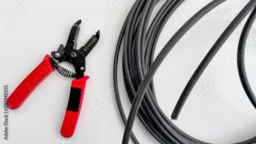 Fotografie Red wire cutter tool next to several black electrical wires top view