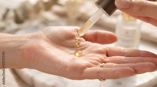 Golden serum drop falling on palm. Applying organic facial oil for skincare routine.