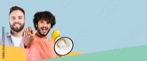 Bild auf Leinwand Excited Young Male With Curly Hair, Smiling And Pointing At Camera While Holding A Megaphone In A Studio Setting