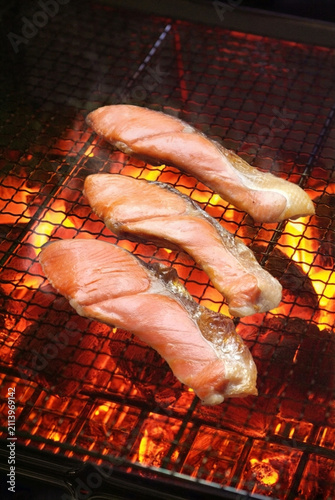 天然ベニザケの切り身を網に載せて炭火で焼いているスモーキーな料理写真