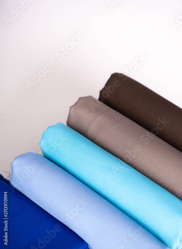 A crisp studio shot displaying a neat collection of colorful fabric rolls in blue, brown, and grey, perfect for textile design, crafts, and apparel manufacturing