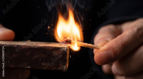 A close-up shot of hands striking a match to ignite a flame, with sparks flying.