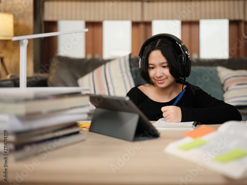 Asian teenage girl concentrates on online class, remote learning at home using tablet, writing and reading textbooks, self-study for back to school, Homeschooling, university education lifestyle.