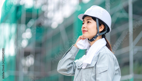建築現場の足場をバックにタオルで汗を拭うヘルメット姿の女性作業員（労働・安全管理）