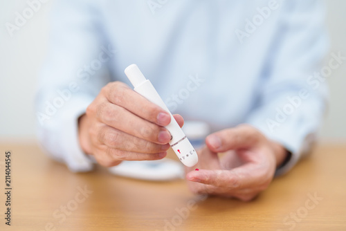 Foto Hand using lancet pen on finger with Blood drop glucose testing or Diabetes checking by digital blood glucose meter
