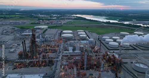 Aerial view of oil refinery with large storage tanks, industrial structures, and pipelines under a sunset sky