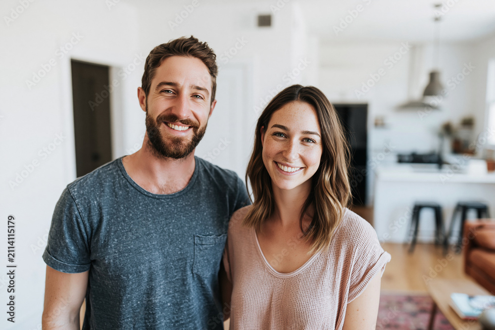 Fototapeta premium Happy couple smiles warmly in bright, modern home. Soft natural light fills open kitchen and living space. Wood floors, minimalist decor, and cozy atmosphere. Perfect for family, home