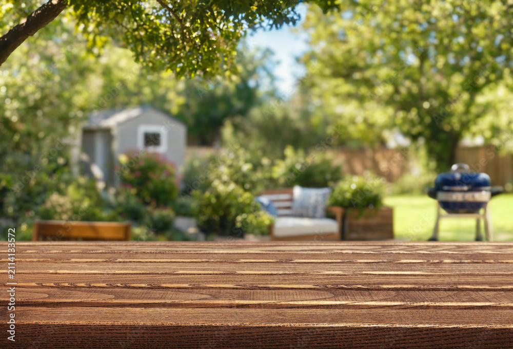 Obraz premium blurred background of a backyard garden with grill BBQ and wooden table on foreground