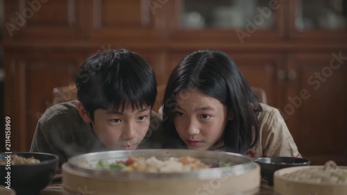 Asian children looking at steaming food in bamboo steamer at home