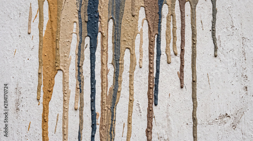 Dried paint drips in mixed colours running down a matte wall surface