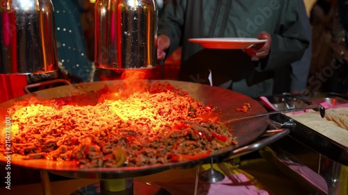Freshly cooked stir fried noodles with beef and vegetables on a large catering flat-top grill.