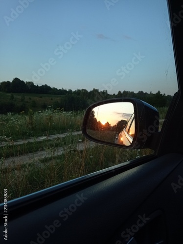 Sunrise reflected in the side window of a dark gray car.