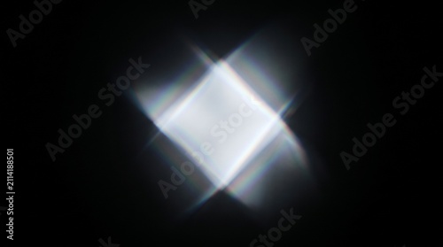 Prism reflection casting a bright white diamond shape with spectral edges onto a deep black background to highlight the beauty of optical physics and light refraction in a clean minimalist.