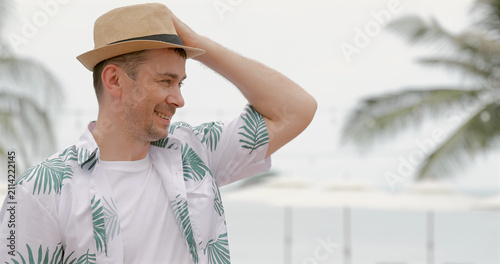 Cuadro en lienzo Man in hat wearing tropical shirt, smiling outdoors with palm trees in background, embodying vacation, relaxation, tropical getaway concept