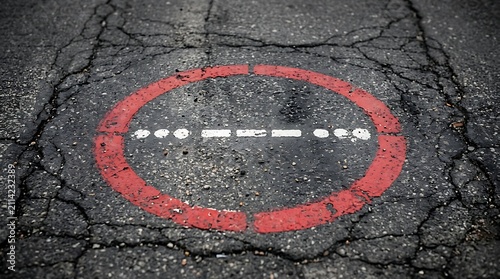 Red circle painted on cracked asphalt road. Warning sign marking damaged pavement surface.