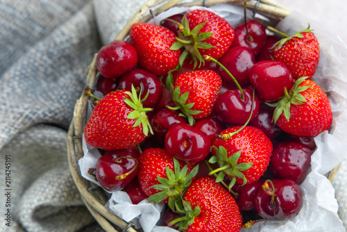 Fresh strawberries and cherries placed in a small woven basket on a soft fabric surface