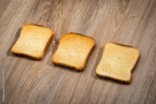 Obraz na płótnie Three golden rusks neatly arranged on wooden surface