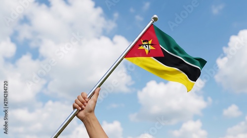 Low angle shot of hand waving Mozambique national flag against sunny blue sky with clouds
