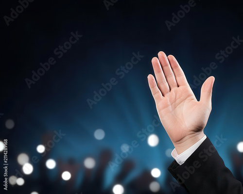 Hand business raised gesture audience light conference suit signals participation during presentation with dark stage background