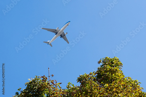 Airplane flying overhead against blue sky with trees below