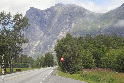 Empty country road surrounded by high mountains and green trees under cloudy sky, Raumadalen, Trollvegen, Andalsnes, Norway