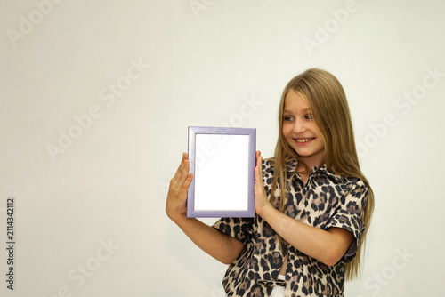 Obraz na płótnie Smiling Girl Showcases a Blank Frame in a Creative Studio Space With Vibrant Ene