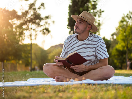 Young man enjoys sunset while reading a book in a park.
