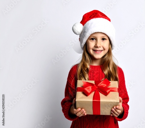 A cute young girl wearing a Santa hat and red sweater holding a gift box.