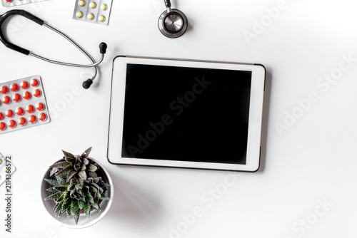 Modern medicine workplace with digital tablet, pills, stethoscope white table flat lay space for text