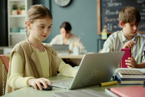 Canvastavla Caucasian schoolgirl using laptop during classroom lesson while classmate checking smartphone, representing digital learning and student technology use